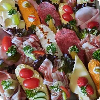Gemischt belegte Brötchen mit Speck, Schinken, mehreren Käsesorten und Aufstrichen, jeweils mit Obst oder Gemüse darauf.